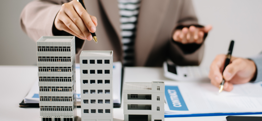 Real estate professionals discussing contract with building model, paperwork, and calculator on table