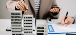 Real estate professionals discussing contract with building model, paperwork, and calculator on table