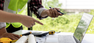 Contractors pointing at laptop screen looking at blueprints